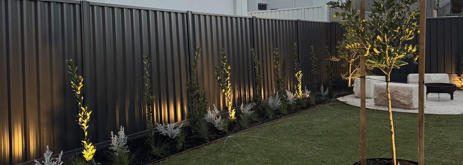 Low-voltage uplighting washing a dark boundary fence and picking out shrubs and a feature tree at dusk in Mullaloo, Perth