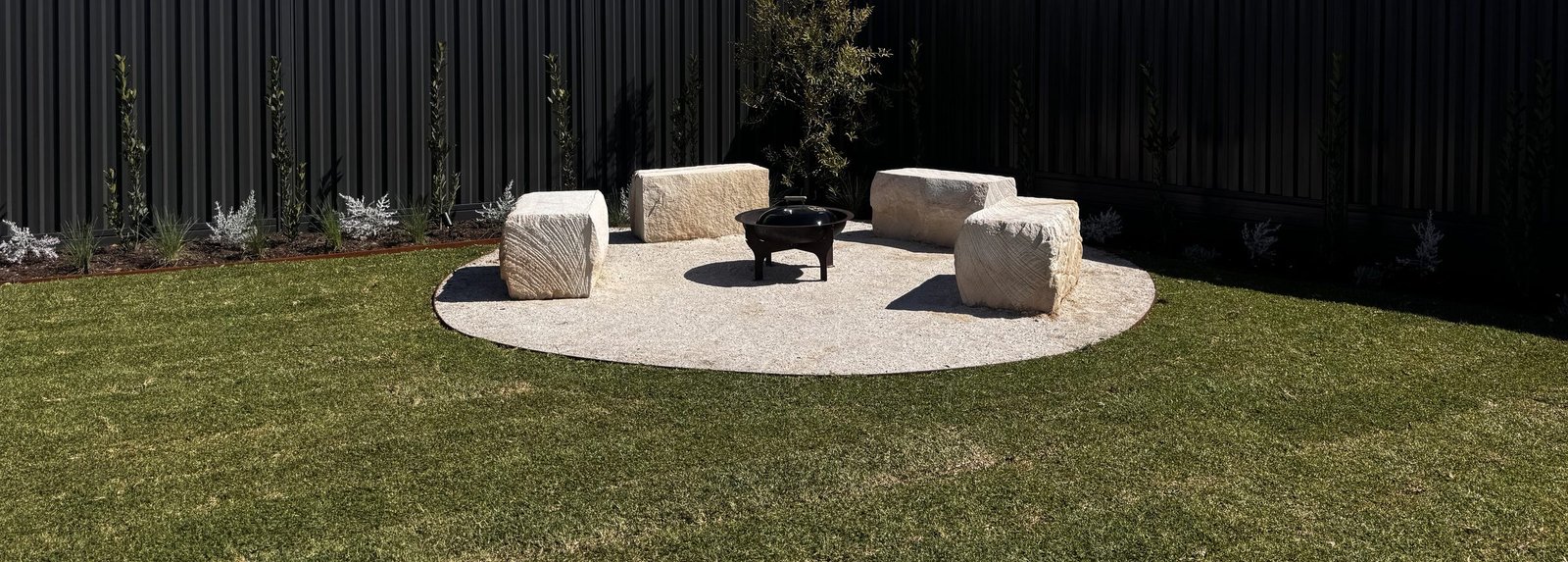 A fire pit ringed by limestone block seating on a circular aggregate pad in a Mullaloo garden by Herbs Coastal Landscapes, Perth