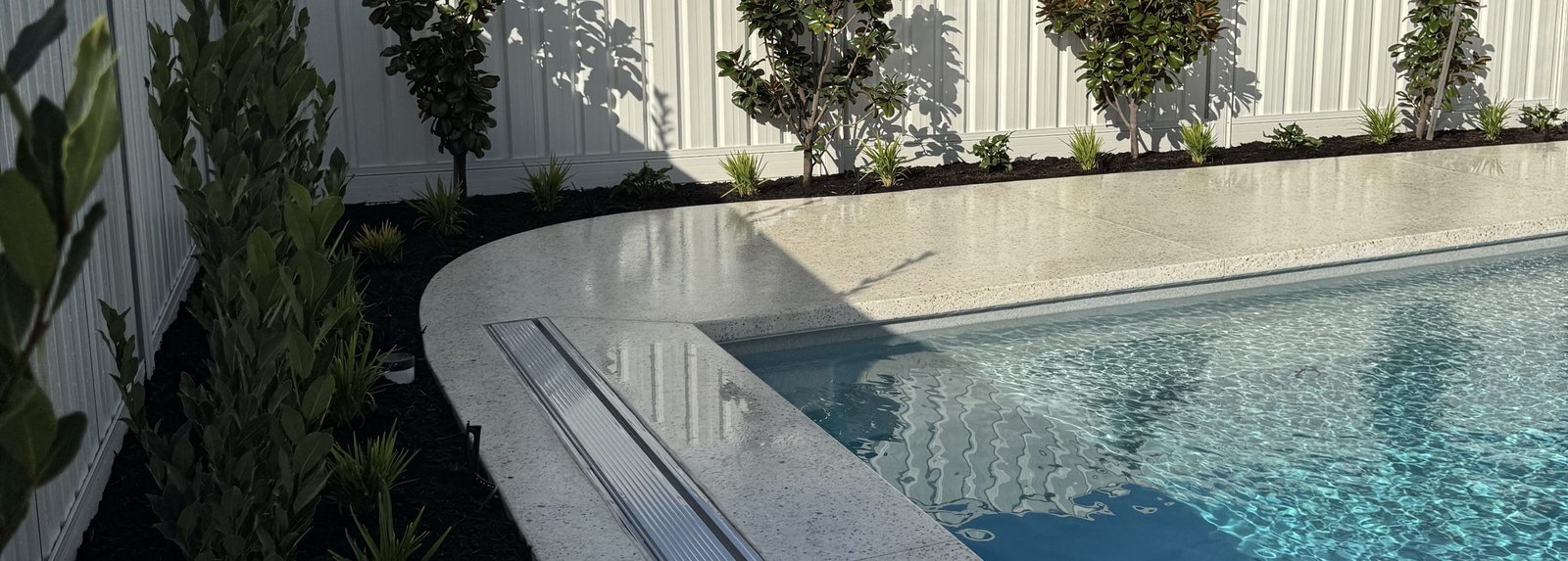 Curved pale concrete pool coping and terrace with screening planting along the boundary, Mullaloo, Perth