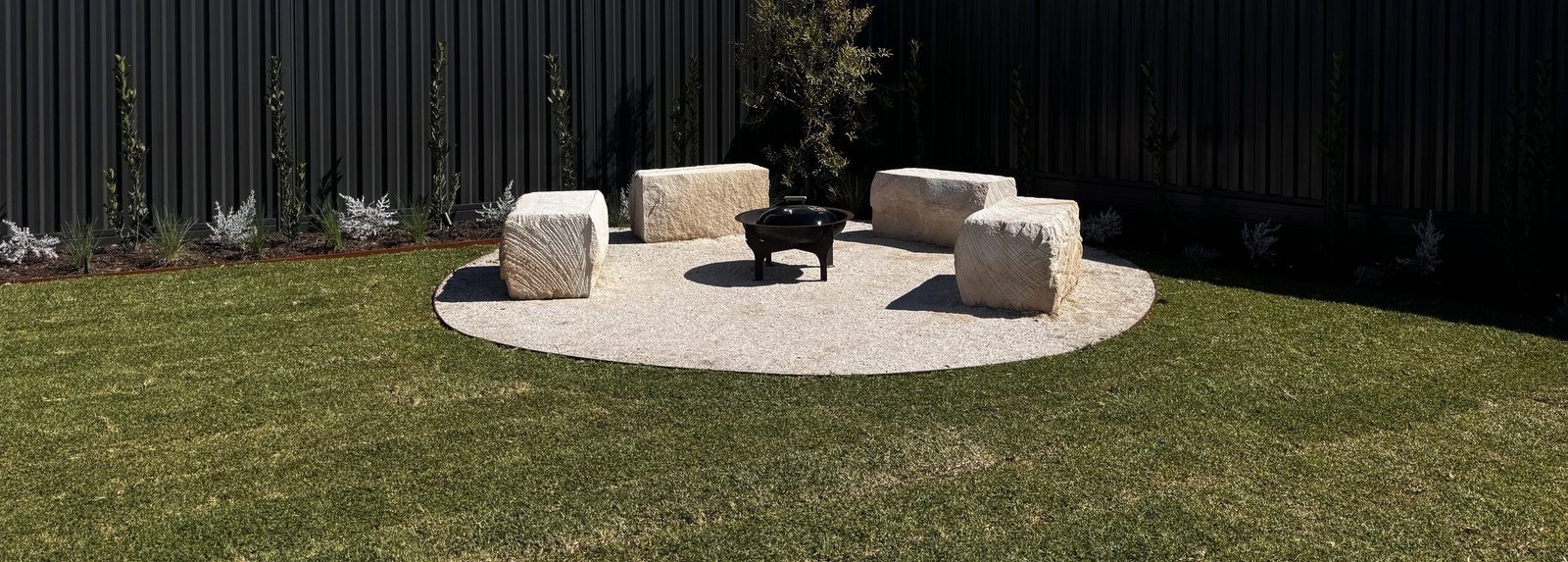 A fire pit ringed by limestone block seating on a circular aggregate pad in a Mullaloo garden by Herbs Coastal Landscapes, Perth