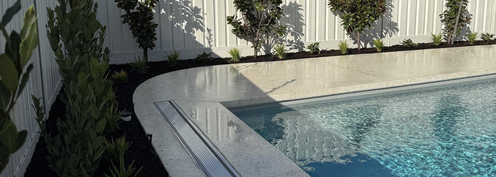 Curved pale concrete pool coping and terrace with screening planting along the boundary, Mullaloo, Perth